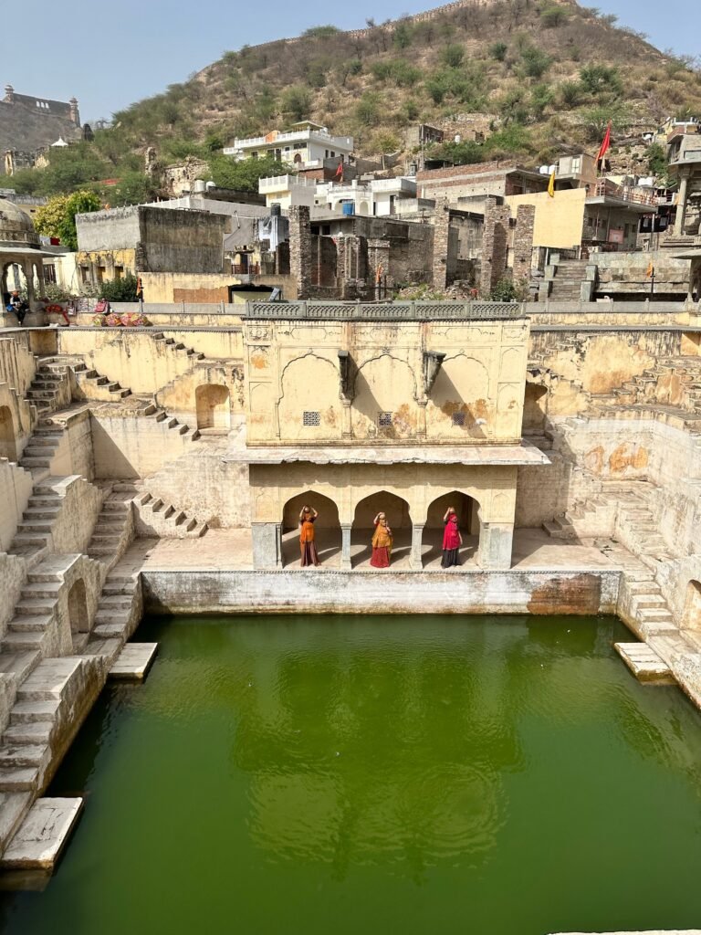 Women in colorful attire standing by a historic stepwell amidst an ancient townscape.